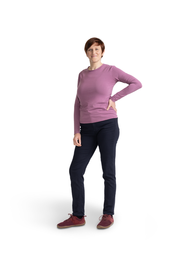 Eine Frau mit kurzen Haaren, dunkler Hose und altrosafarbenem Shirt.